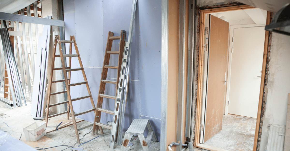 An interior residential remodeling zone featuring exposed wall framing, newly installed purple drywall, wooden ladders, a spirit level, and fine debris on the floor, highlighting the messy phase before hiring professional post construction cleaning specialists.