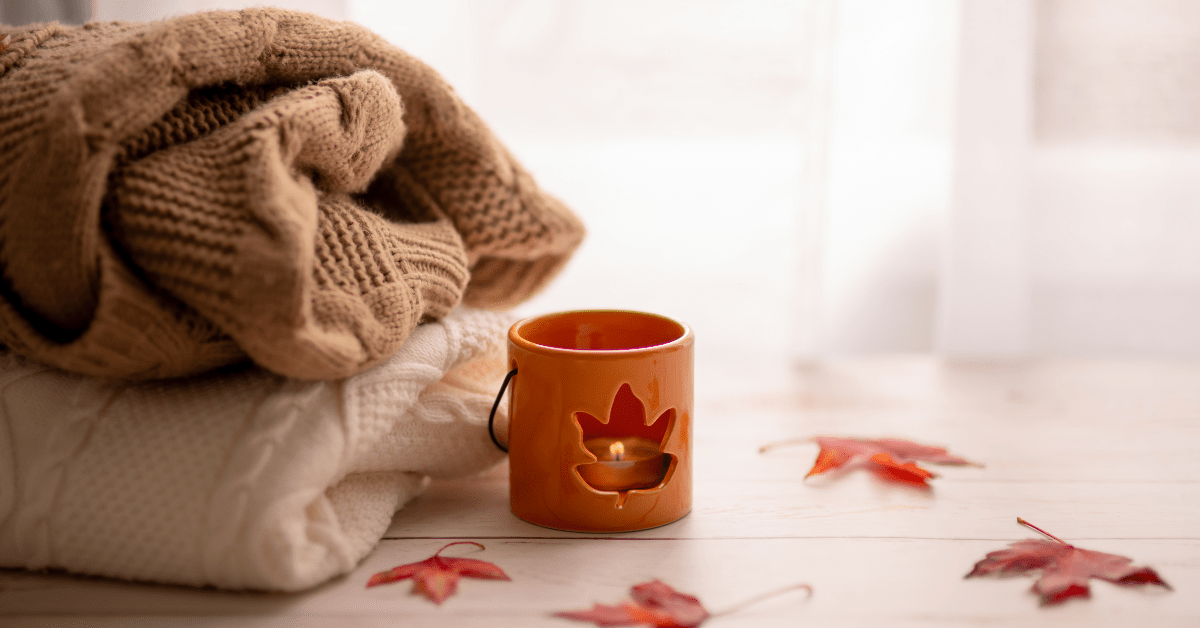 Cozy fall sweaters, autumn candle lantern, and maple leaves illustrating how to prep your home for fall and store summer gear