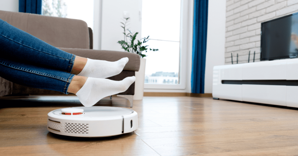 Robot vacuum cleaning a hardwood floor living room while homeowner relaxes illustrating smart home cleaning technology tips